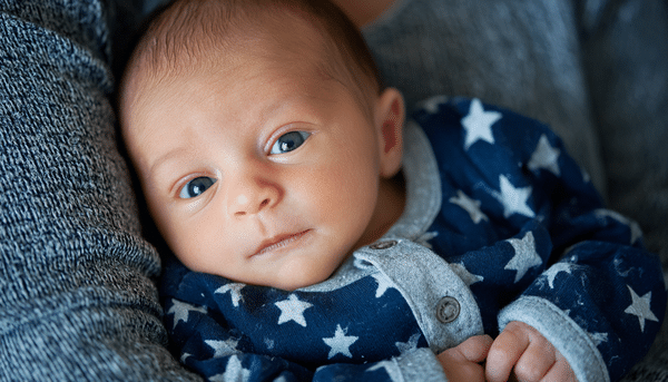 Bebé en los brazos de su madre. El bebé porta una pijama azul con estrellas.
