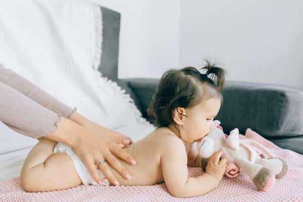 Brazos se una mujer haciéndole un masaje a una bebe de aproximadamente 9 meses de edad. Ambas están en la cama de una habitación.