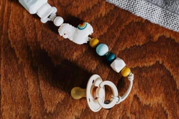 Chupón de bebé en una mesa de madera. El chupón tiene un clip decorado con piedras de color blanco, azul y amarillo.