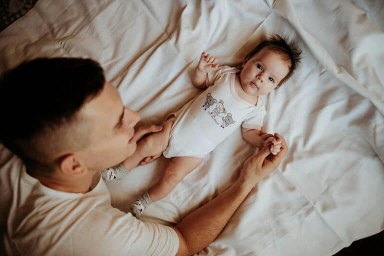 Padre tocando la mano de su bebé que permanece acostado en la cama. El padre parece estar contento.