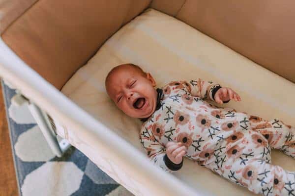 Bebé llorando dentro de su cuna, recién despertando de su sueño.
