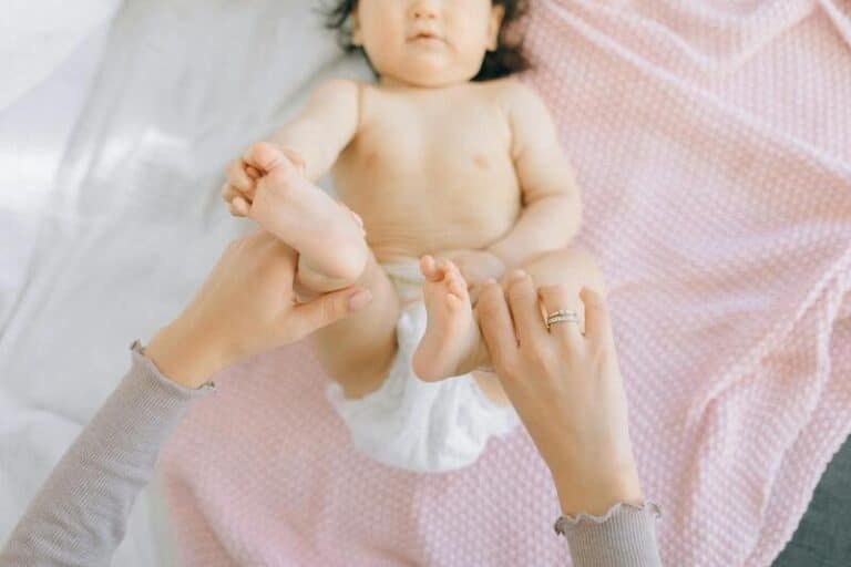 Pequeña bebé recostada en la cama mientras le cambian el pañal.