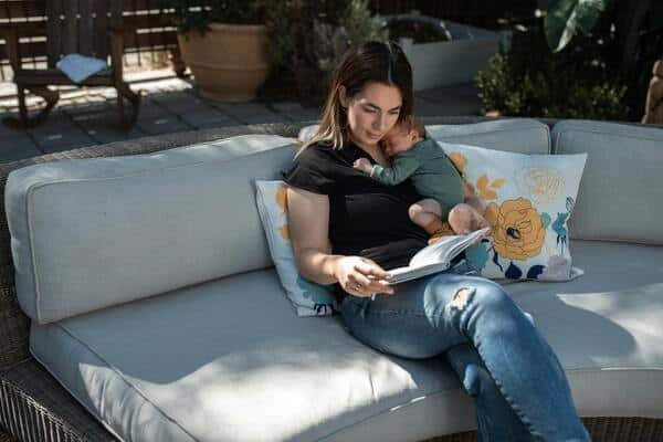 Madre carga a su bebé recién nacido mientras lee un libro. Ambos se ven cómodos y relajados.