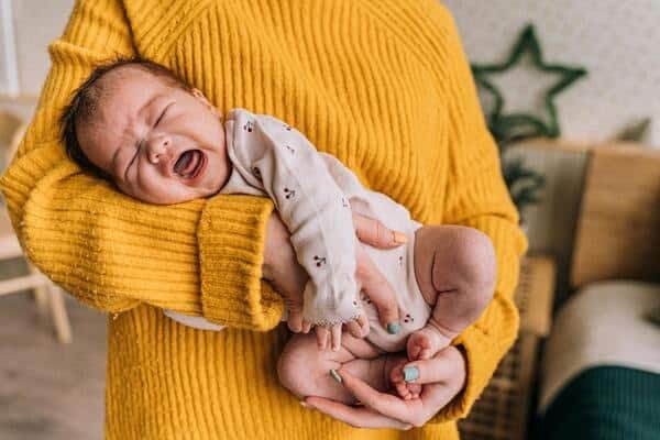 Bebé de pocos meses de edad llora en los brazos de su madre.
